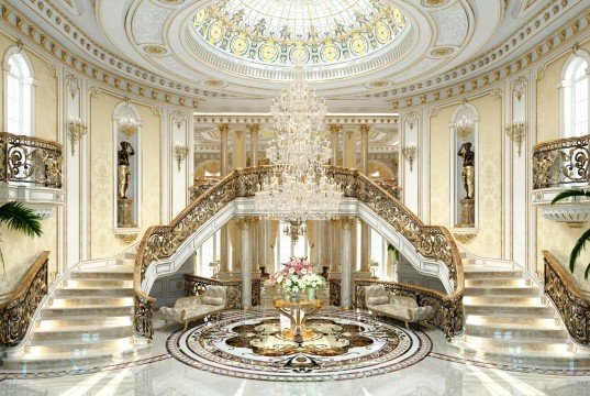 This picture shows a luxurious dining area with a marble dining table and chairs, surrounded by white walls with custom-made artwork. The floor is a light-colored parquet that complements the marble and the walls. There is a crystal chandelier hanging from the ceiling, adding to the elegance of the room. On the walls, there are also luxury built-ins and shelves with ornate decorations.