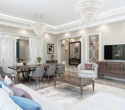 This picture shows an ornately designed and decorated living room with a golden-brown color scheme. The furniture is composed of white tufted sofas and armchairs, a coffee table in the middle and dark brown wooden side tables. The walls are decorated with gold-framed art and mirrors and the window is framed by heavy cream colored curtains. The floor is comprised of a mix of light and dark tiles.