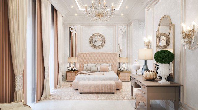This picture depicts a luxurious bedroom interior with a beautiful canopy bed. The bed has a flowing white bedspread decorated with two large, patterned pillows and a plush blanket. On either side of the bed are matching bedside tables and wall lamps with decoratively designed pulled shades. Above the bed is a white sheer canopy with scalloped trim. The walls in the room are a light greyish blue color, with a plinth shelf running along the length of one of them and an ornate decorative mirror hanging above it. The floor is finished in a light wood laminate and there