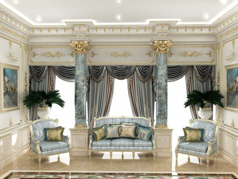 This picture is of a luxurious living room designed in a contemporary style. It features a large floor-to-ceiling window with light grey drapes, two tan colored sofas with white and brown throw pillows, a glass coffee table with a silver base, a metal end table with a blue vase, and a white rug. There is also an elaborately designed white and gold wall decor piece above the sofa.