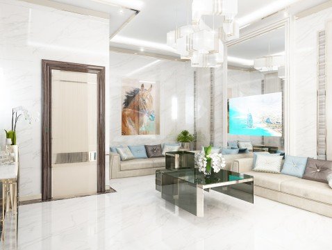 This picture shows a modern styled bedroom with a unique bed frame and headboard. The bed is covered in a white, luxurious looking fabric with silver accents. The walls are painted in a light grey color with a large paneled mirror mounted along one wall. A window is visible with silver curtains hung around it, giving the space a modern and sophisticated feel. There is an upholstered ottoman at the foot of the bed, providing a convenient seating area. A few plants are also seen, adding a natural touch to the room.