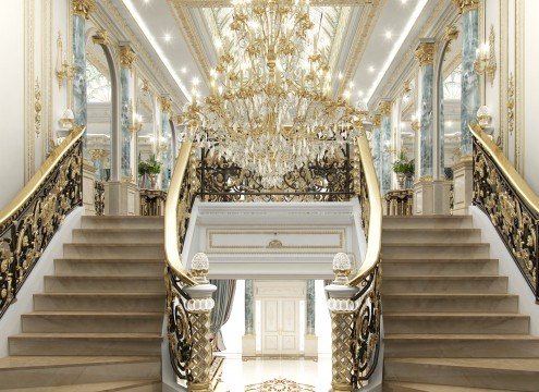 This picture shows an ornately decorated marble staircase with stone columns and balustrades in the middle. The staircase is outlined with a gold railing and leads to a landing on the second floor. At the top of the stairs, a large chandelier hangs from the ceiling, with intricate designs adorning the walls. The overall effect is one of luxury and grandeur, indicative of traditional European architecture.