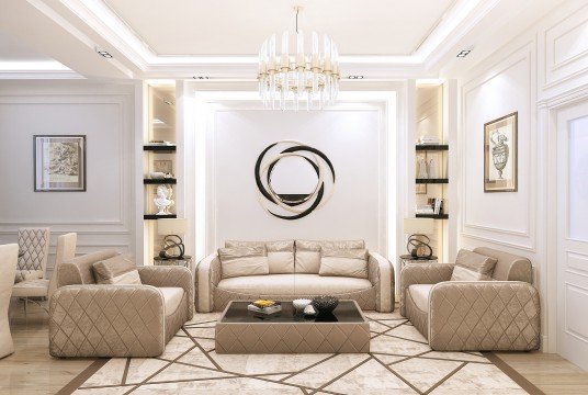 This picture shows a luxurious living room interior with a white and gold color scheme. The walls are painted white, and the ceiling is decorated with ornate gold designs. The room has white and grey marble flooring, velvet couches, a light grey rug, and two gold accent chairs. There is also a contemporary fireplace with a gold mantelpiece and two gold wall sconces on either side. On the mantlepiece, there is a large centerpiece that is made of white stones. In the center of the room, there is an elegant glass coffee table with a white and gold base