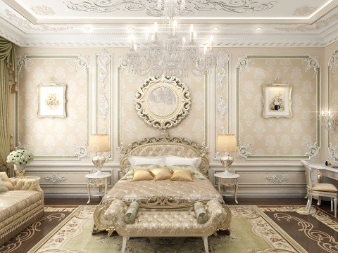 This picture shows a luxury hotel lobby with high ceilings and ornate decor. The space is filled with furniture pieces made from luxurious materials, ranging from velvet couches to marble tables. The walls of the lobby are covered with dark wood wainscoting and white columns, complemented by a large chandelier and greenery along the walls. There is a large rug in the center of the room, as well as a grand staircase leading up to an upper level.