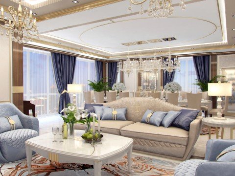 This picture shows a luxurious master bedroom with a grand king size bed and headboard. The walls are painted a beige color, and the ceiling is adorned with decorative gold trim. There is an elegant array of brocade pillows and throws on the bed and also on the two lounge chairs situated in front of the bed. The floor is carpeted in a shade of light grey, and there is a round wooden table and a large ornate mirror between the chairs. There is a pair of tall golden lamps on either side of the bed, adding to the overall glamour of the room