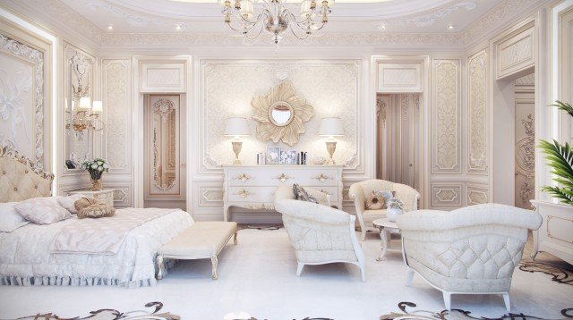 This picture shows the interior of a luxurious and modern bedroom. The walls are painted a light beige, and there is a large patterned carpet on the floor. There is a bed with a dark wooden headboard and white bedding, two bedside tables with lamps, and an armchair in the corner. The furniture has intricate carvings and detailed design, adding to the luxurious feel of the room. The walls are decorated with paintings and pictures, and there is a window that lets in natural light.