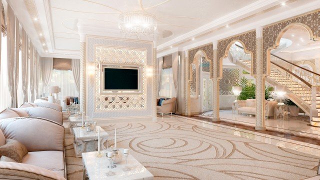 The picture shows a luxurious small hallway with white marble walls and a large, gilded mirror in the center. The floor is lined with a luxurious light gray carpet and the walls feature two decorative sconces. An elegant white circular bench is positioned against one wall and a tall, slender plant stands in a corner.