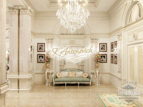 This picture shows a luxurious and modern hallway in an upscale home. The hallway features a curved staircase with a brass banister, a chandelier, and a marble floor. The walls are also adorned with elegant artworks and sconces. The hallway appears to be very spacious, giving it a grand look.