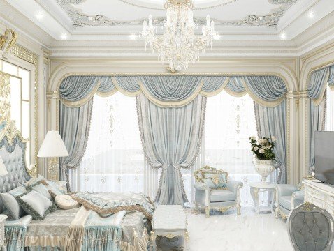 This picture shows a luxurious living room with a white marble floor, champagne colored walls and a crystal chandelier. The furniture is upholstered in beige fabric and includes two couches, two armchairs, a glass coffee table, and a round ottoman upholstered in velvet. The room is decorated with a vase of flowers on the coffee table and a golden mirror on the wall.