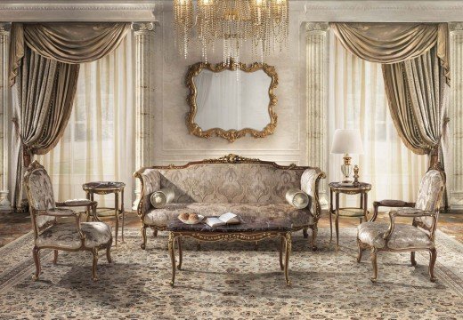 This picture shows a luxurious bedroom, with a modern four-poster bed in the center. The bed is dressed in light colored fabric and topped with an ornate wooden canopy. On each side of the bed are matching nightstands with crystal lamps, while at the foot of the bed is a patterned gray ottoman. The walls are painted a soft off-white and accented with wall sconces and mirrors. The room is further accented by the addition of bright pillows on the bed, a fur throw blanket, and a potted plant for a hint of