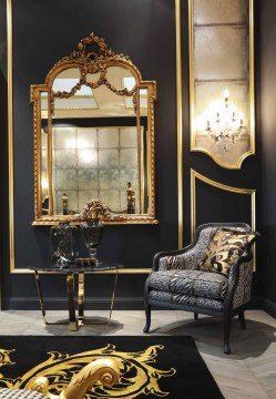 This picture shows an ornate, luxurious bathroom with beige marble walls and floors. There is a double sink set in a large countertop with a gold-framed mirror above it. To the right of the sinks is a walk-in shower with an elegant rainfall showerhead and additional body sprayers on the wall. The corner of the room is filled with a free-standing bathtub with a golden ornate faucet. On the floor are plush beige towels and a luxurious white rug.