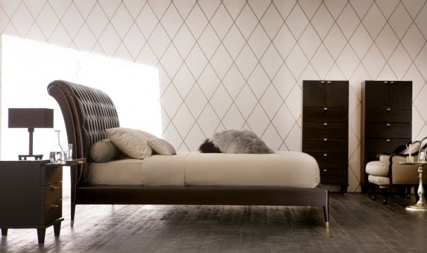 This picture shows a large open living area with light cream colored walls and a tiled tile floor. There is a sectional sofa in the center of the space with two armchairs on either side, all finished in white leather. A white velvet tufted coffee table sits in the middle of the seating area, with a modern cylindrical-shaped chandelier overhead. Two tall glass doors are visible on the left wall, leading out to a balcony that overlooks the city skyline.