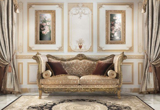 This picture shows a stairwell in an elegant home. It has a light-colored carpet running down the stairs, matching with the white walls of the staircase and the light fixtures on the wall. At the foot of the steps is a beautiful round table and chairs, surrounded by large windows that look out over a garden.