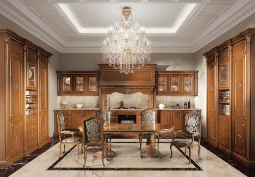 This picture shows a luxurious, modern living room with a variety of high-end furniture pieces. The sofa and chairs are upholstered in a white and tan fabric, with intricate patterns, and have gold accents and legs. The fireplace has a marble surround and is topped with a large mirror. There are two end tables with marble tops and gold legs, as well as a round coffee table with a marble top and gold base. A large, patterned rug is the centerpiece of the room and the walls and ceiling are painted a creamy white.