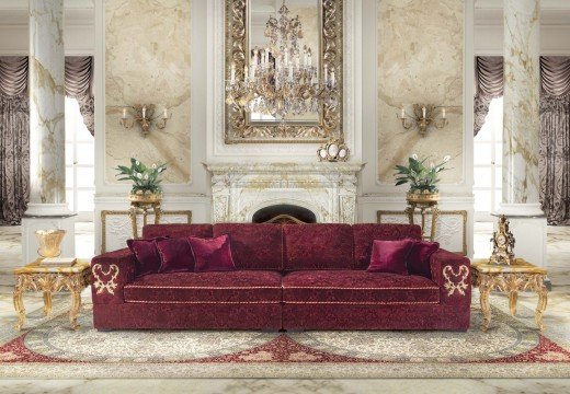 This picture shows a luxurious living room with a beautiful marble floor and beige walls. The room has two white sofas and two wooden armchairs, adorned with white and beige pillows. There is a wooden and marble coffee table, and a stone fireplace with a large ornate mirror and vases on either side. At the back of the room is a large window with white shutters that allow light to filter in.