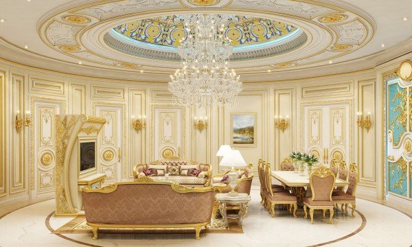 This picture shows a luxurious and modern living room. The room has beige walls, a light wood floor, and a white ceiling with a beautiful chandelier. The furniture pieces in the room are composed of a two-seater sofa, two armchairs, and a round glass-top coffee table. The walls are lined with colorful abstract paintings, and there is an orange rug in the center of the room.