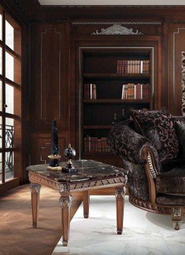 This picture shows a luxurious bedroom with marble walls, a floor-to-ceiling window with drapes, a modern white and gold headboard, and a brown loveseat flanked by two large royal blue velvet armchairs with gold accents. A large round glass chandelier hangs from the ceiling and a round ottoman sits in the center of the room. A wooden dresser and a beveled mirror are also seen in the room, along with a few pieces of wall art.