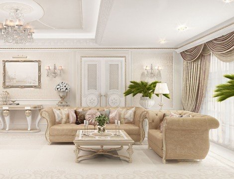 This picture shows a stunning living room in an upscale home. The room has pale wood floors, white walls, and an off-white suede sofa with rose gold accents. There is a round dark wood coffee table with a white ceramic lamp and decorative accent pieces on top. A floor-to-ceiling white window stretches across the back of the room and provides plenty of natural light. A wall-mounted flat-screen television is mounted on the wall and two modern armchairs with patterned cushions are situated around the coffee table. A large abstract painting hangs over the sofa, adding