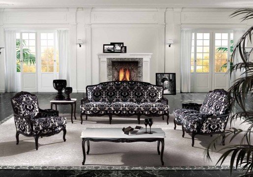 jpgThe picture shows a living room designed with a rustic theme. The room features a dark wood floor and cream-colored walls, giving the space an atmosphere of warmth and comfort. In the foreground, there is a comfortable gray couch with several decorative pillows, flanked by two side tables with lamps. Behind the couch are two bookshelves filled with books and other items. The centerpiece of the room is a large stone fireplace, flanked by two wooden armchairs. On the right side of the room is a large window, providing natural light and a view of nature outside.