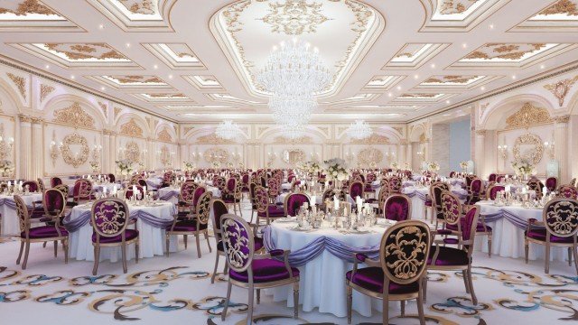 This picture shows a modern, opulent entrance hall in an Arab-style mansion. The space has multiple levels, with sleek white marble floors and walls, detailed gold accents, modern furniture, and a stunning chandelier at the center of the room. A set of grand stairs leads up to a higher level, where two beautiful gold-accented arches can be seen.