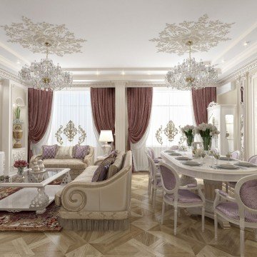 This picture shows a luxurious living room with a white and gold color scheme. The room contains a white sofa with lot of cushions, two armchairs in gold patterned fabric with matching footstools, and a stunning round brass table. There is a large white rug on the floor, and a beautiful chandelier hanging from the ceiling. On the walls are white curtains and gold-framed pictures.