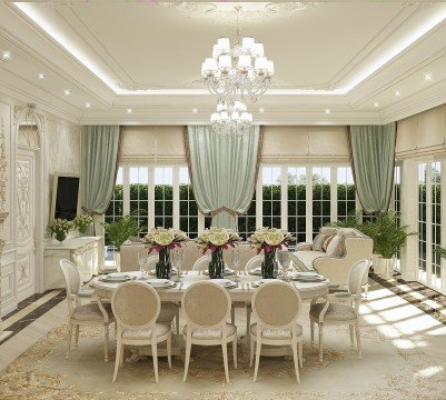 This picture shows a luxurious, modern living room. The room is decorated with high quality materials and includes a cream leather sectional couch, two beige armchairs with ottomans, a glass topped coffee table with a chrome base, and an off-white area rug. The wall is adorned with a beautiful abstract artwork, and several small potted plants provide a splash of color to the neutral tones. Large windows let in natural light, and there are several floor lamps scattered around the room to provide additional lighting.