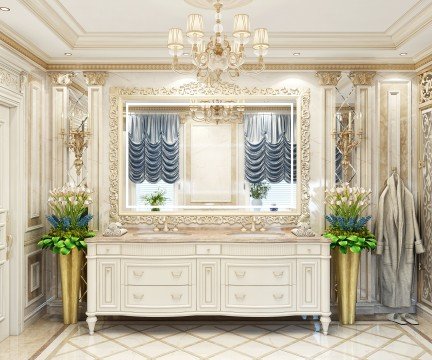 This picture shows a modern luxury bedroom with a large, four-poster bed in the center of the room. Above the bed hangs a large, ornately-framed mirror, and next to the bed are two bedside tables topped with elegant lamps. The walls of the bedroom are painted in a soft grey color with white crown molding, and the floor has light wood paneling along with a richly patterned rug.