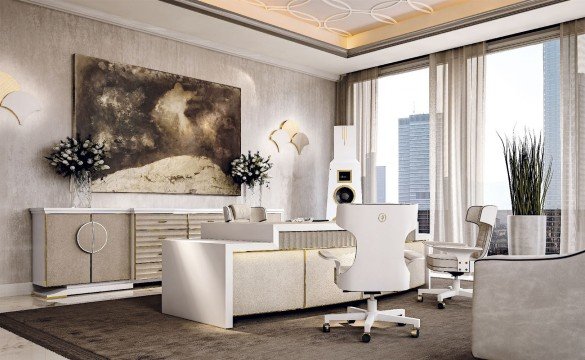 This picture shows a modern, luxurious living room designed in shades of cream, beige, and brown. The room contains two comfortable sofas upholstered in light brown with matching ottomans, a center table with a white marble top, two armchairs upholstered in beautiful patterned fabric, and a unique, curved accent wall behind the seating area. Other features in the room include an ornate crystal chandelier, textured wallpaper, and an abstract art piece hung above the sofa.