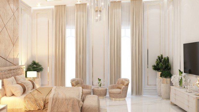 This picture is of an elegant living room designed by Antonovich Design. The room features a comfortable seating area, with a white tufted sofa and two armchairs upholstered in a cream fabric, centered around a glass-top coffee table with gold accents. The room is decorated with a large crystal chandelier, beige and gold décor pieces, and framed artwork.