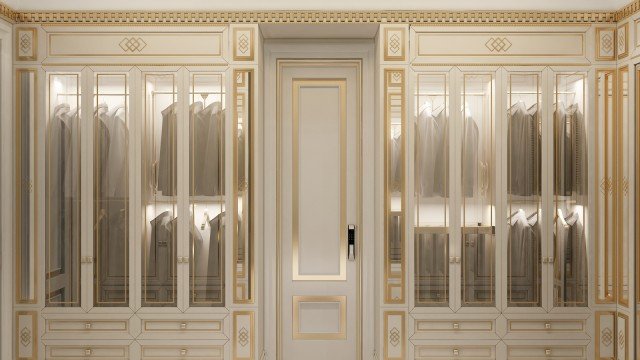 This picture shows a grand, double door entryway. The doors are made up of ornately carved wood and are surrounded by white marble columns. Above the doors is a domed ceiling painted in gold and decorated with intricate geometric patterns. There are two wall-mounted lamps on either side of the entryway, which cast light onto the steps below.