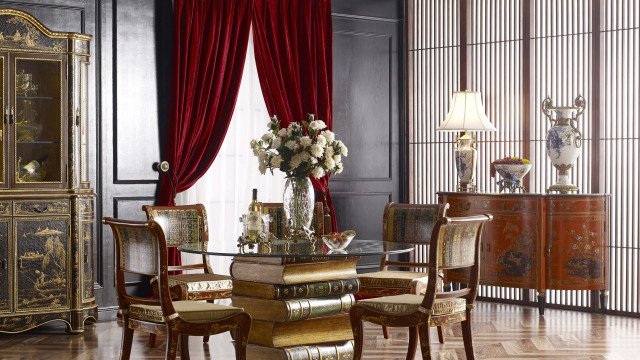 This picture shows an elegant, contemporary living room with a white-and-grey color scheme. The room features two white velvet sofas facing each other, a white marble coffee table, and a white rug adorning the floor. A large bookshelf filled with plants and books is placed against the wall, while a modern glass chandelier hangs from the ceiling. The room has large windows which allow natural light to flood the space.