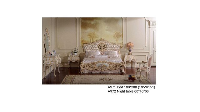 The picture shows a luxurious interior of a high-end bedroom. The room has a very large canopy bed with a white upholstery headboard. On either side of the bed are two columns with a sparkling chandelier above it. There is a grand floor to ceiling window that provides a view of the beautiful outdoor scenery. On the left side of the bed is a comfortable armchair upholstered in white fabric. The walls are painted in a warm beige colour and there are several pieces of stylish artwork on the wall. On the right side is an ornate vanity with