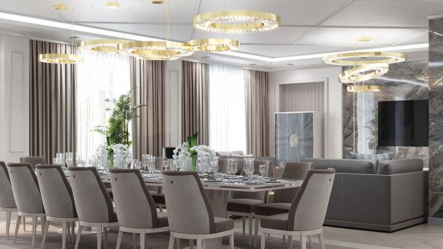 This picture shows an ornately decorated dining room. The floors are a dark wood and there is a large crystal chandelier hanging from the ceiling. The walls are painted a pale cream color as is the ceiling, with gold trim around the edges of the walls. There are two chairs upholstered in a deep ruby damask set against the wall, and a side table in between them with a white marble top.In the center of the room is a large dining table with an intricate base and a black marble top. On the table is a bouquet of pink roses, a