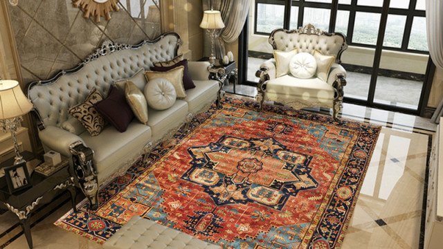 This picture shows a luxurious living room in shades of cream and gold. The room has a large cream-colored sofa with padded armrests and a striped pattern on the upholstery. There is an ornate gold coffee table in the center of the room, with an intricately patterned rug below it. The walls are adorned with painted stripes and a large painting of a sunset, while the window is draped in sheer white curtains. A round chandelier hangs from the ceiling, providing a soft light to the room.