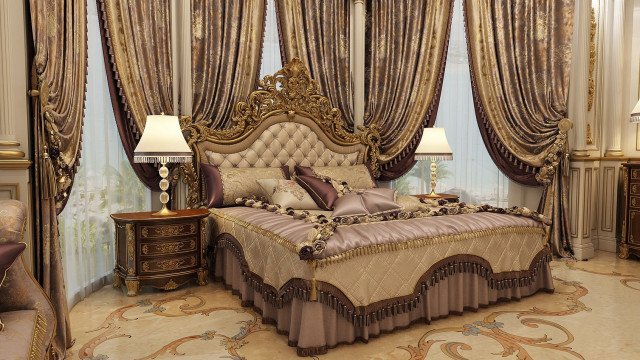 This picture shows a luxurious bedroom with an extravagant crystal chandelier. The bedroom features a tufted velvet headboard and an elegantly upholstered bench at the foot of the bed. The walls are painted in a deep, navy shade and are accented with wall sconces. The carpet is plush and luxurious, and there is a matching area rug situated beneath the bed. The lighting fixtures and fixtures draw attention to the room's ornate decor.