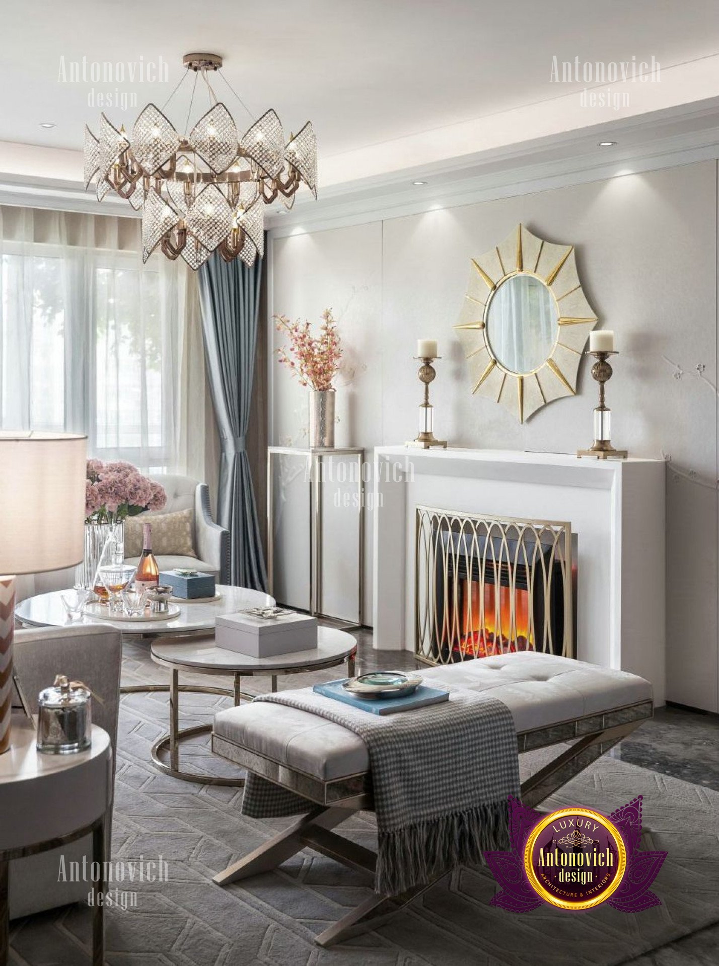 This picture shows a grand entryway in a luxurious home. It features marble flooring, ornate walls and an archway with a built-in fireplace that is framed with gorgeous columns. There are two large, elegant staircases flanking the fireplace with intricately carved balustrades. On either side of the entryway, there are high windows with swags and tassels. There is also a large chandelier that hangs from the center of the archway.