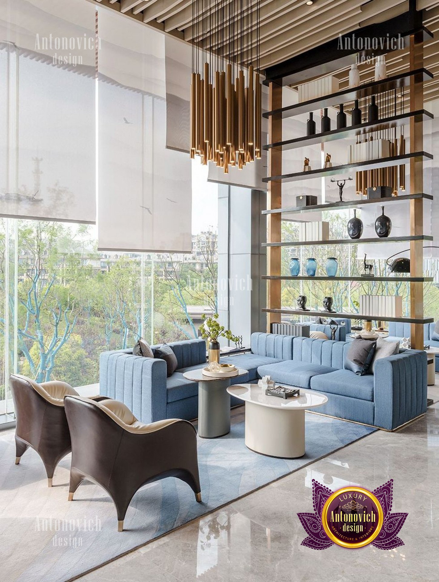 The picture is of a luxurious modern living room. It features a white sofa and chair set, with a grey accent wall in the background. The flooring is a light hardwood, and a white marble area rug is featured in front of the sofa. On either side of the sofa are glass and metal end tables with white lamps on them. Also in the room are two tall bookshelves filled with books and decor, as well as a few abstract art pieces on the walls.