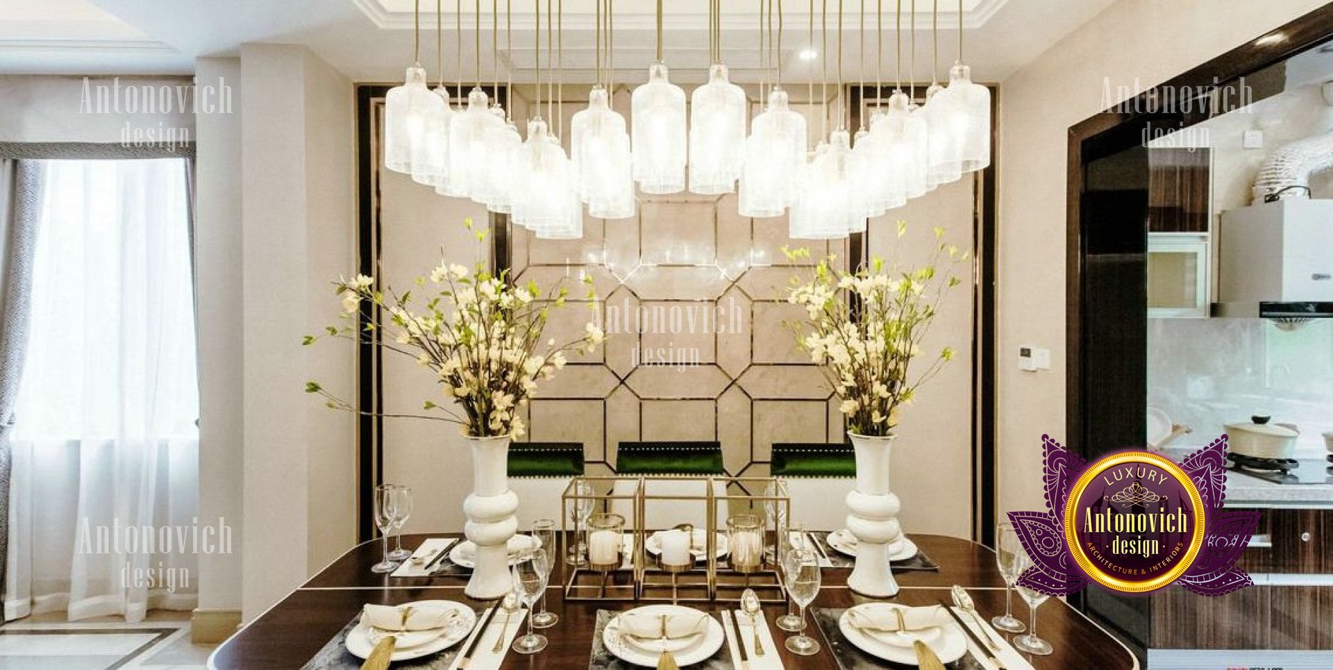 This picture shows a luxurious living room designed with a classic, modern look. The walls are decorated with a gold print wallpaper with symmetrical designs on it and there is a large crystal chandelier in the center of the ceiling that casts a warm light over the room. The furniture includes a plush navy velvet sofa with cushions covered in gold and white accent pillows, a light gray armchair, and a wooden glass-top coffee table. The floor is tiled with marble and there is a large area rug in the center of the room that brings out the colors in the decor.