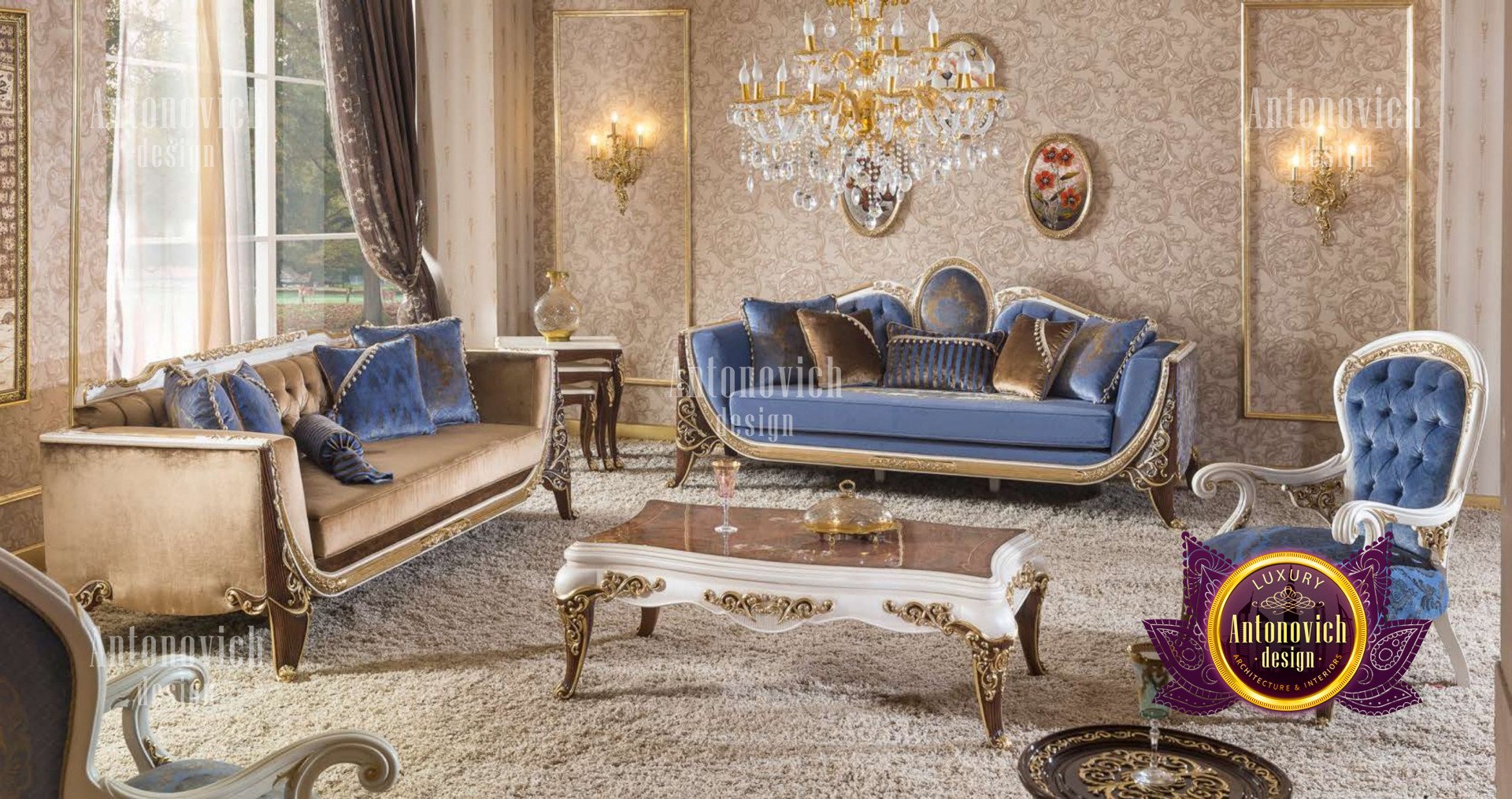 This picture shows a luxurious, modern living room designed by Antonovich Design. The room is decorated in white and gold, with ornate wall panels, a crystal chandelier, and white marble flooring. The furniture in the room is upholstered in a bright blue fabric and is arranged in a symmetrical pattern. A large, framed painting hangs on one wall, and two identical side tables are placed near the sofa.