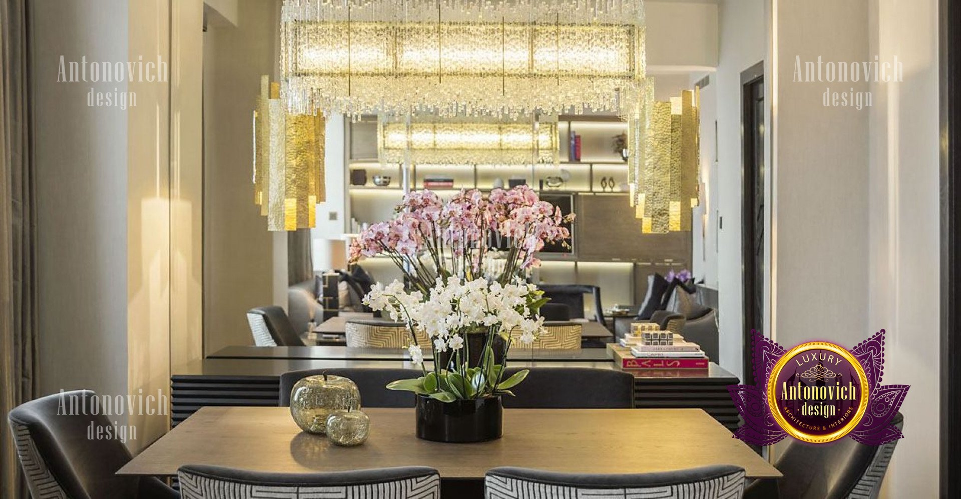 The picture shows a luxurious home office designed by Antonovich Design. This modern office features floor-to-ceiling windows, light wood floors, and white walls to make the room feel bright and airy. The large wooden desk is finished in a dark espresso and is surrounded by an elegant white armchair and two sets of matching bookshelves. The desk also has several drawers and cabinets for storage and organization. The light fixtures are modern and sleek, adding to the sophisticated atmosphere.