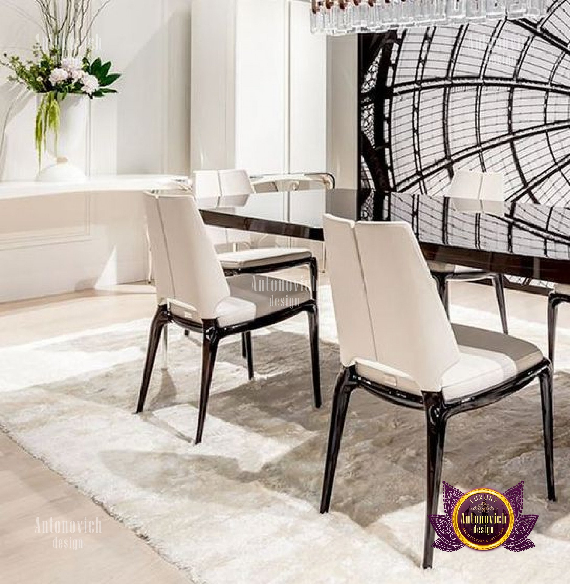 This picture shows a modern interior design featuring a black and white color palette. In the foreground, there is a large sofa with a plush grey rug beneath it, and two white armchairs on either side. There is also a white coffee table in the center of the room and a black dining table with chairs on the left. On the right, there are built-in cabinets with a variety of decorations on top, including a vase of white flowers and a ceramic pot. On the wall behind the furniture, there is a large framed painting with an abstract pattern in shades of grey and white