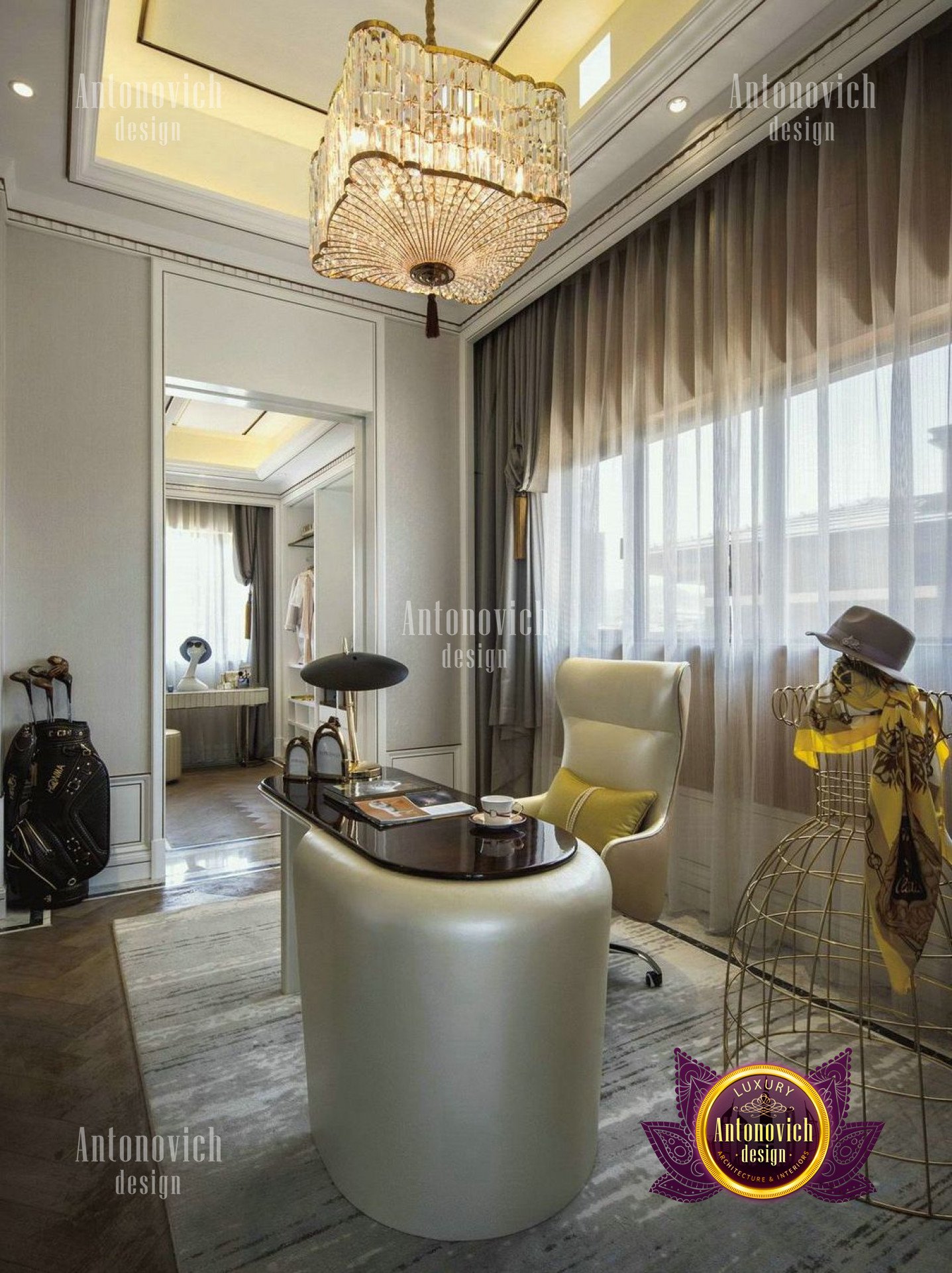 This is a picture of a modern, luxurious living room with mostly white and grey tones. The walls are adorned with light grey wallpaper with silver accents and the floor is covered with a white area rug. There is a long, sleek white sofa with several decorative cushions, and a beige velvet armchair in the corner. On either side of the sofa are two wooden tables with glass tops. A large painting of a peaceful cityscape hangs on the wall, and several framed photographs are scattered around the room. The finishing touches are delicate metal sculptures and several potted plants.