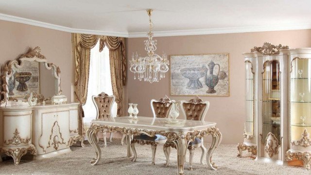 This picture shows a luxurious interior design that features a large cream-colored sofa and armchairs with intricate designs. The walls are painted a light grey color, while the floor is made up of dark hardwood with ornate rug designs. The room has a grand yet cozy feel, with two grand lamps and unique end tables to complete the look.