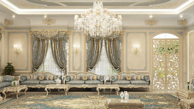 This picture shows a luxurious living room designed by Antonovich Design. The room has a beige and white color scheme, with ornate decorations, furniture, and accessories. The room features a grand marble fireplace, a crystal chandelier, neoclassical-style furniture, a marble coffee table, patterned curtains, and golden accents. The room also has several art pieces throughout, as well as a large area rug in the center.