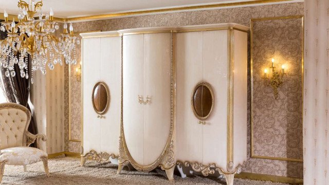 This picture shows an elegantly designed stairway with a curved wooden railing, grand marble steps, and intricate beige and gold details. The railing is ornately detailed with a combination of beige and gold-colored scrolls and accents, while the steps are made of a glossy black and white marble. At the top and bottom of the stairs, two ivory balconies provide additional space for seating and decorations.