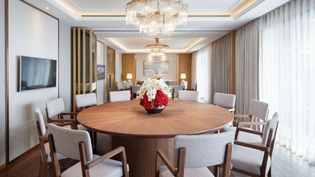 This picture shows an ornate modern living room designed by Antonovich Design. The room is decorated in luxurious materials such as marble, gold, and velvet. There is a central seating area with two large furniture pieces, an armchair and sofa, facing each other. The walls are covered with golden wallpaper with intricate patterns and tiles. The ceiling is also decorated with gold accents and features a large, ornate chandelier. A variety of decorative accents, such as vases and sculptures, can be seen throughout the space.