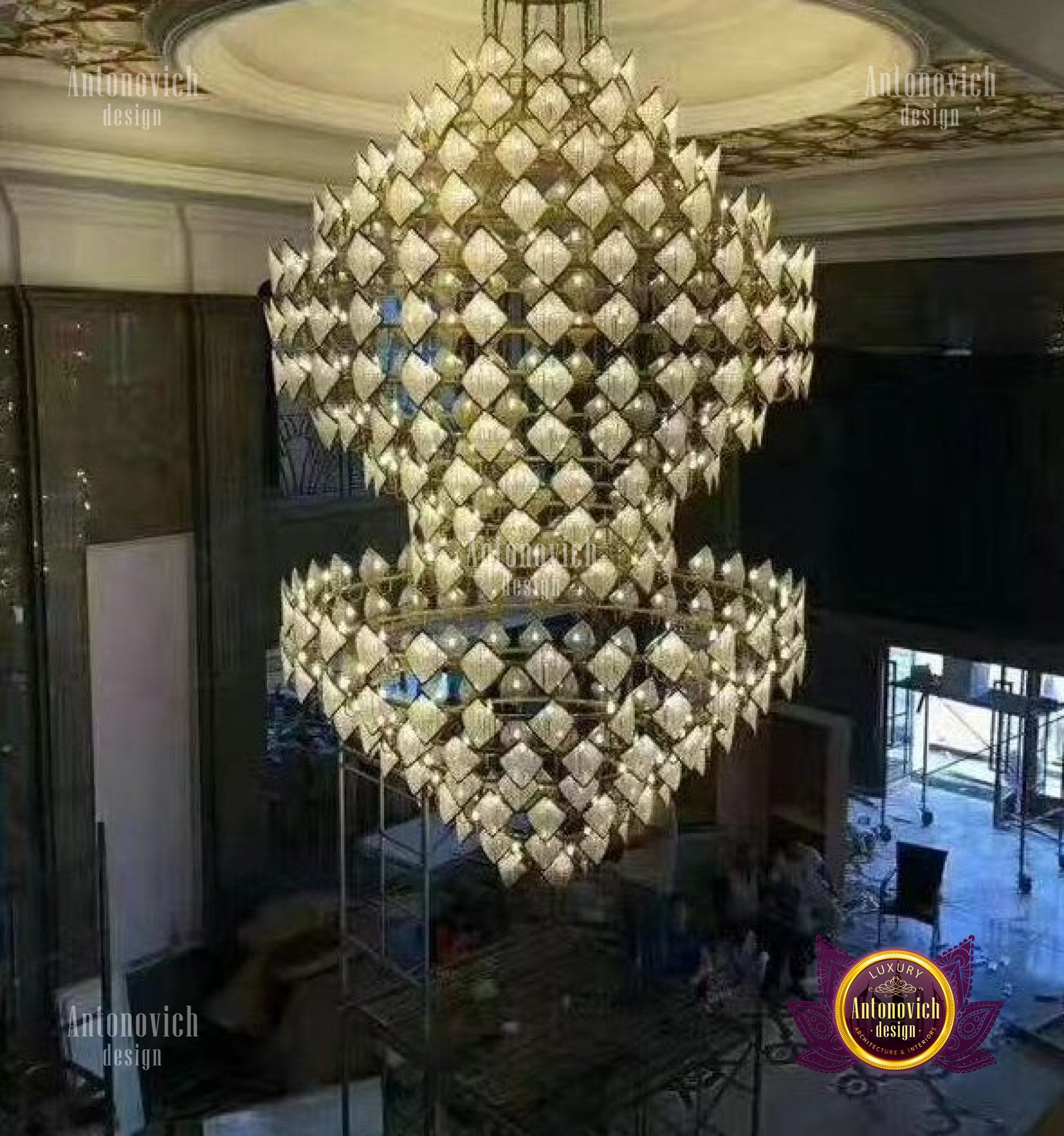 This picture appears to show a formal dining area in an elegant home. The room features a circular wooden dining table surrounded by eight chairs upholstered in plush velvet fabric. An ornate chandelier hangs from the ornately decorated ceiling, providing light to the room. The walls of the room have intricate crown molding and there is a patterned rug covering the floor.