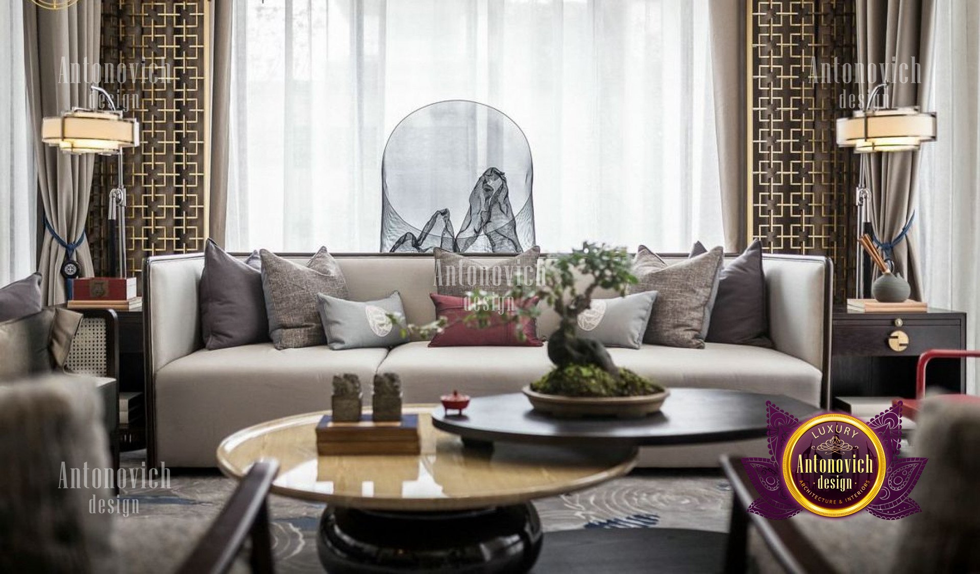 This picture shows a modern living room with an angled ceiling. The walls and ceiling are painted in light beige, while the floor is covered in dark wood. The room features an L-shaped grey sofa, with two armchairs placed opposite it. A coffee table is situated in front of the sofa and there is an abstract painting on the wall behind it. The ceiling has several recessed lights, as well as a chandelier.