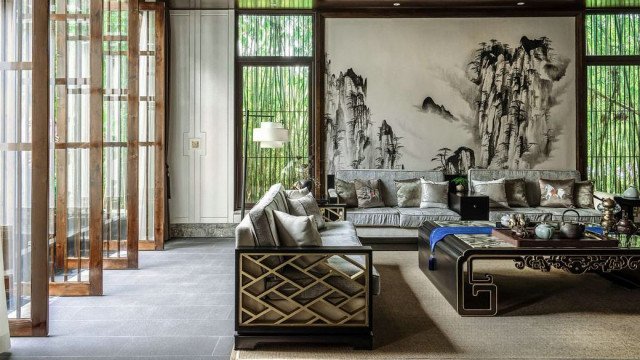 A luxury living room featuring an ornate ceiling, wall-mounted light fixtures, upholstered chairs, and a white checkered rug.