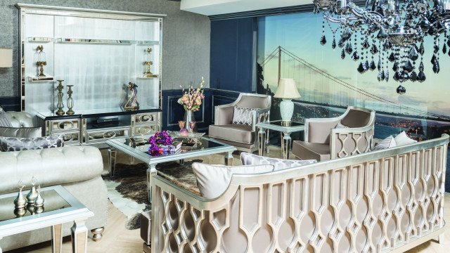 Modern living room featuring wood flooring, high ceilings with elegant moulding, sectional couch, round coffee table, and accent wall in neutral color.